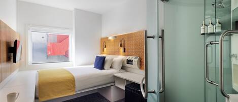 A compact hotel room with a bed, bedside table, and a small desk with a chair.