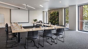 A modern conference room with a long table, black chairs, a projector screen, and a large plant wall. - BreakFree on Cashel Christchurch (Christchurch)