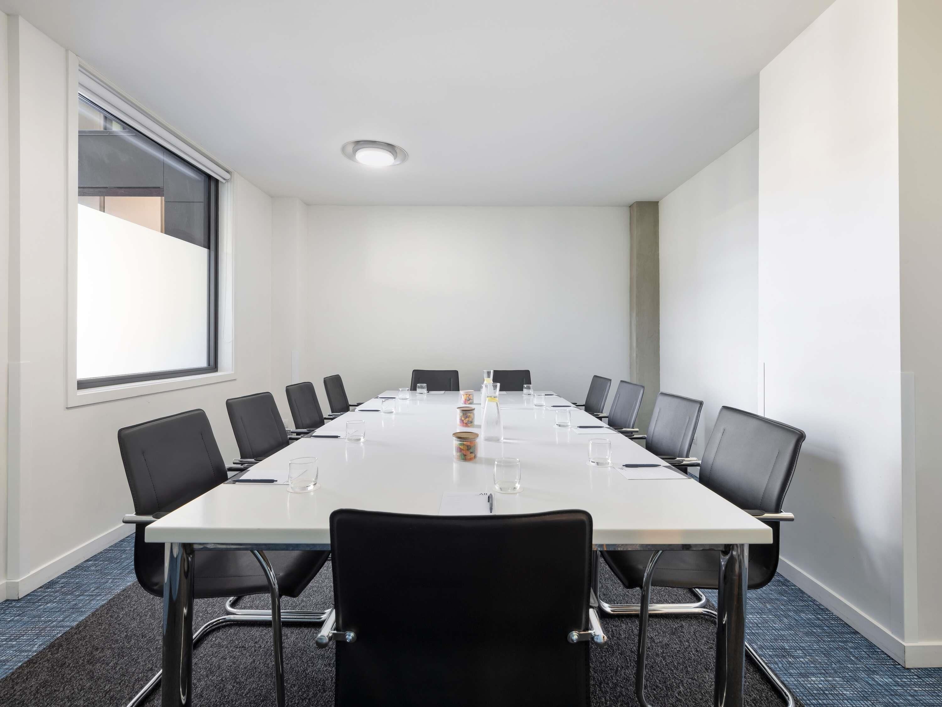 A conference room with a long table, black chairs, and a large window.