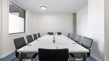 A conference room with a long table, black chairs, and a large window.