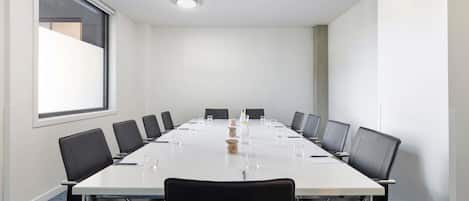 Un salón de conferencias con una larga mesa, sillas negras y un amplio ventanal.