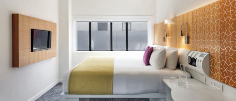 Ein modernes Hotelzimmer mit einem Bett, einem an der Wand montierten Fernseher, einem Nachttisch mit Lampe und einem Fenster mit Jalousien.