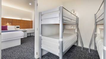 Quarto com beliche, cabeceira branca, mesa de cabeceira com abajur e carpete estampado.