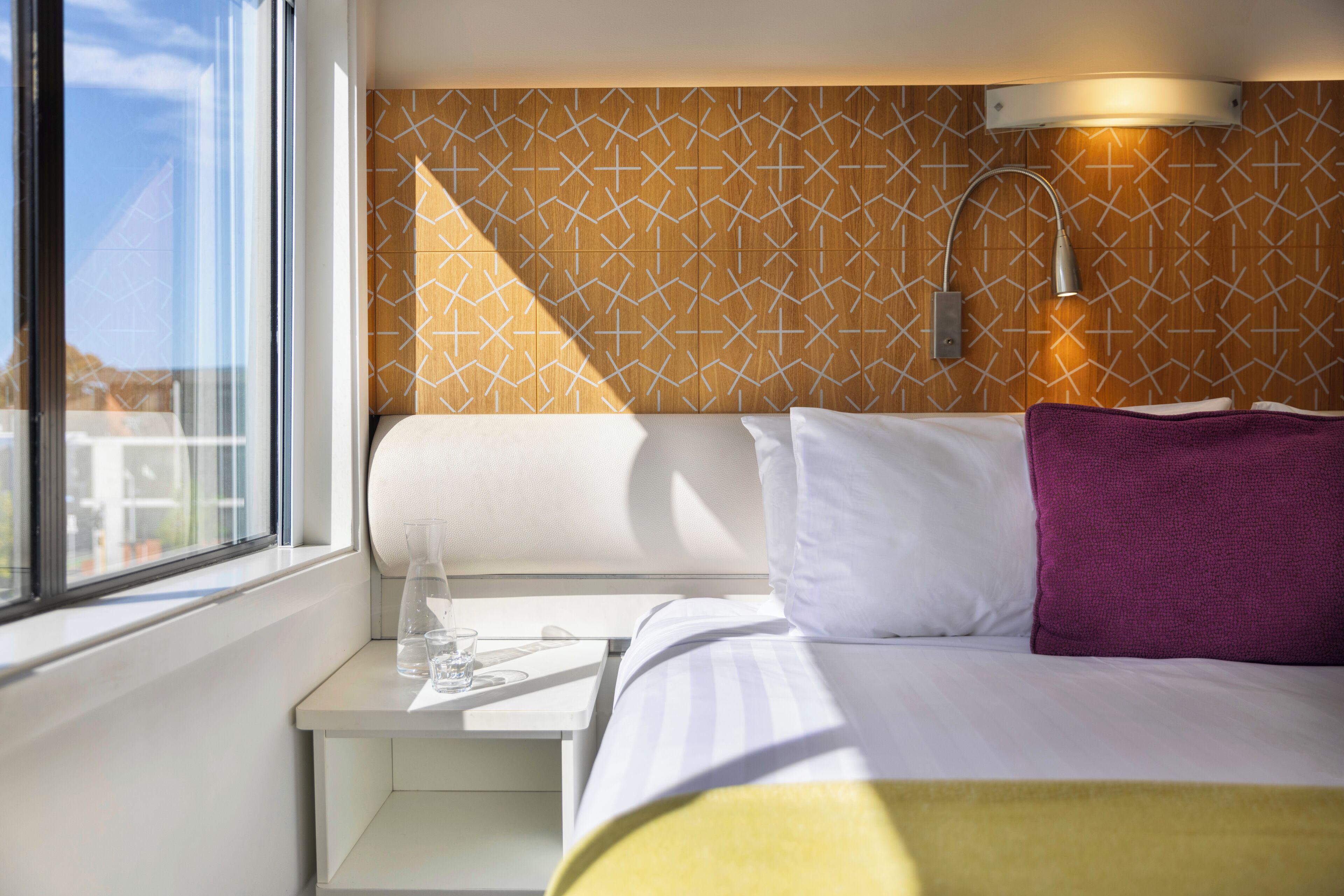 A hotel room with a bed, bedside table, lamp, and a window with a view.