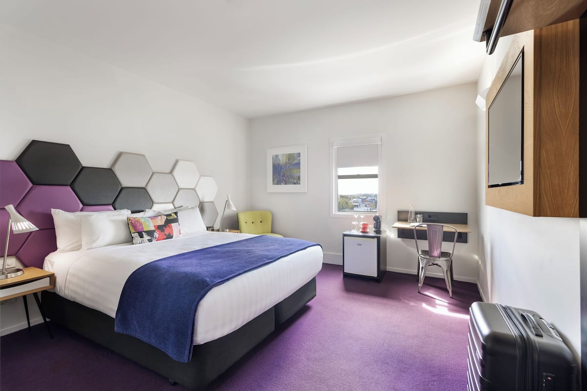 Una habitación de hotel moderna con una cama, un escritorio, una silla y una maleta.