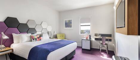 A modern hotel room with a bed, a desk, a chair, and a suitcase.