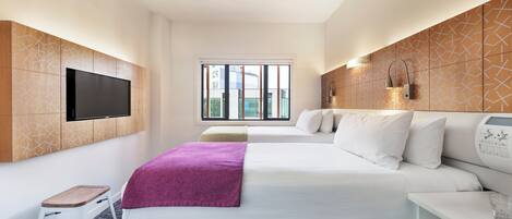 Une chambre d’hôtel avec un grand lit, un téléviseur fixé au mur, une fenêtre avec vue et une table de chevet avec une lampe.