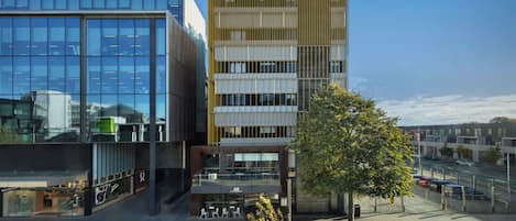 A modern building with a glass facade, a wooden panel design on the upper floors, and a tree in the foreground.