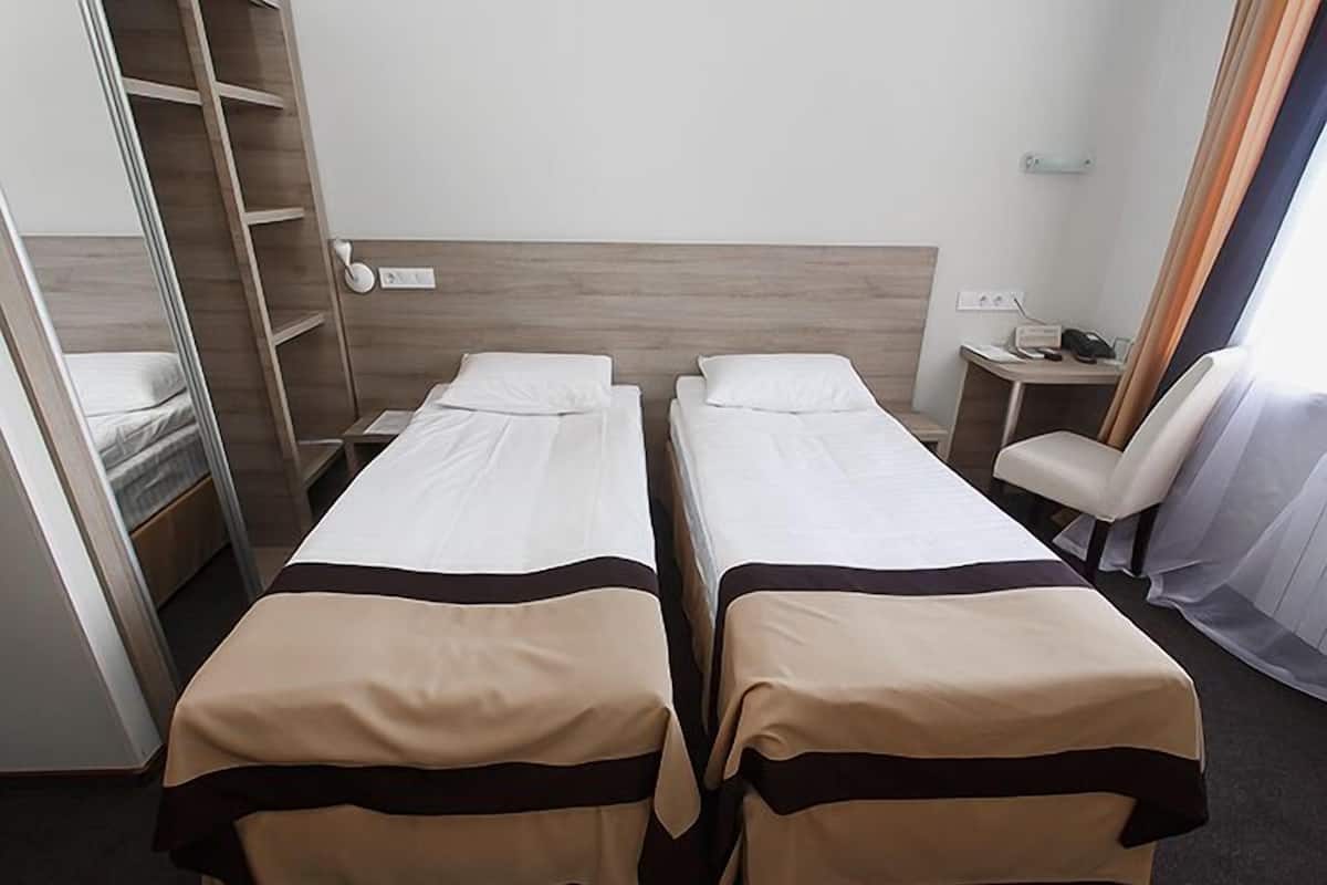Une chambre d’hôtel avec deux lits simples, une armoire, un bureau avec une chaise et une fenêtre avec des rideaux.