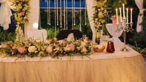 An outdoor wedding setup with a table adorned with flowers and candles, draped in white fabric.