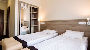 A hotel room with two single beds, a wooden headboard, a wardrobe, and a mirror.