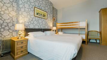 A neatly arranged bedroom with a large bed, bedside lamps, a wooden nightstand, a radiator, a bunk bed, and a chair.