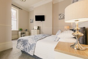 Un dormitorio con cama, mesita de noche, lámpara, televisor, cómoda y ventana.