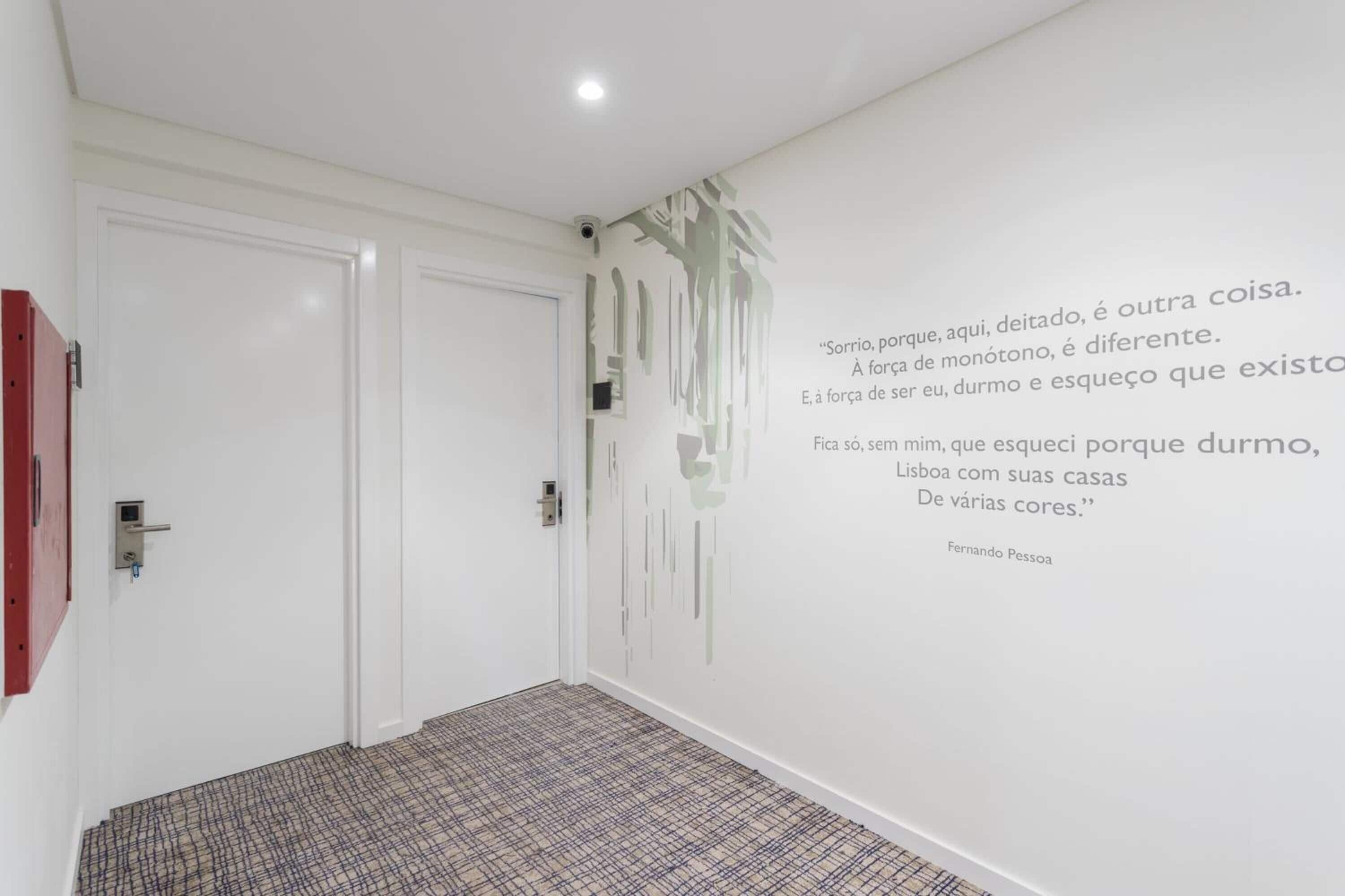 Un corridoio con una moquette a fantasia, pareti bianche e una citazione di Fernando Pessoa.