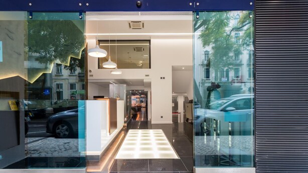 A modern hotel entrance with a glass facade, a reception desk, and a visible interior corridor. - Hotel Capital (Lisbon)