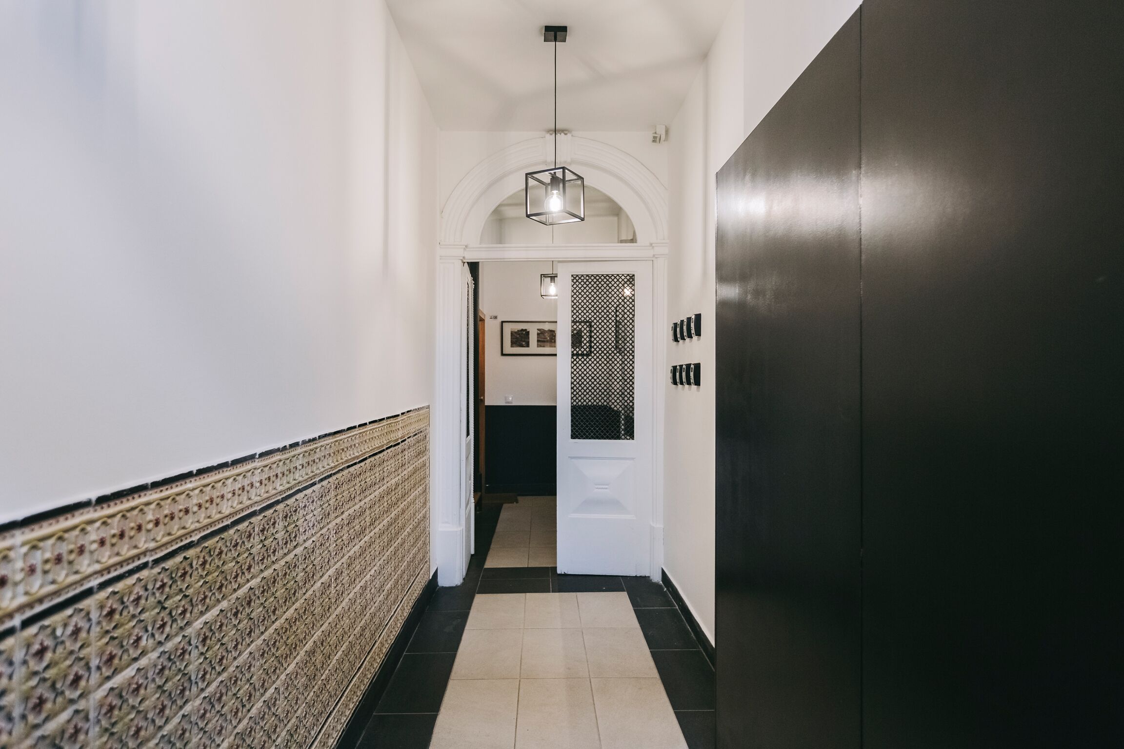 A hallway with a patterned wall, a black door, and a hanging light fixture.