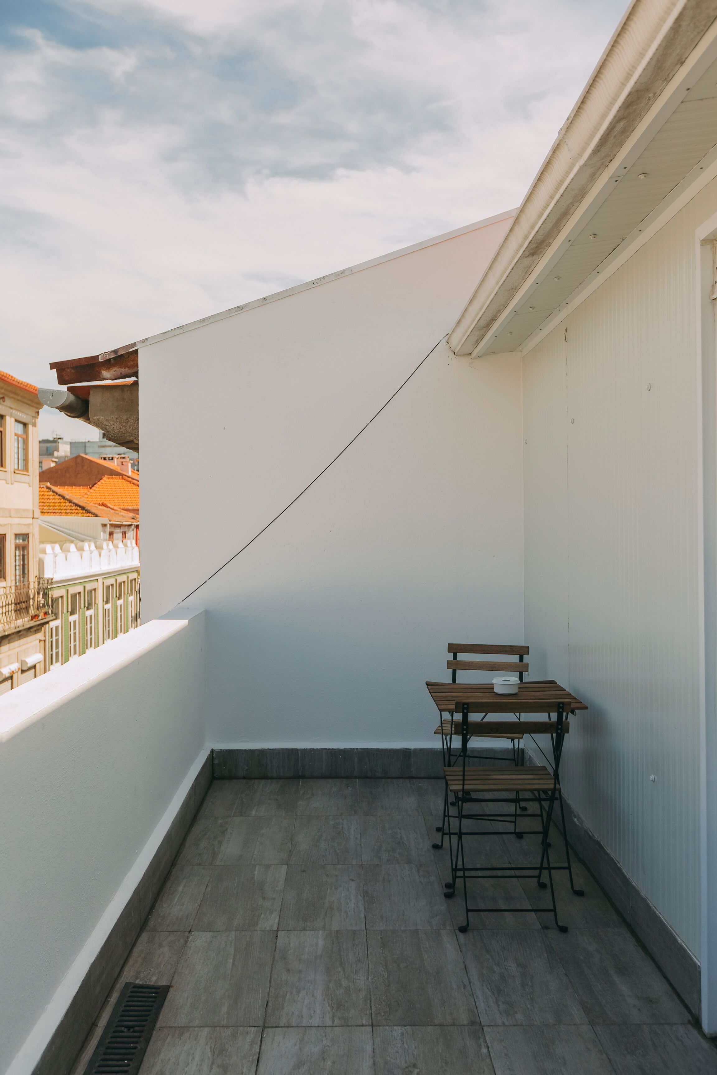 A balcony with a table and chairs, a drain, and a view of buildings.