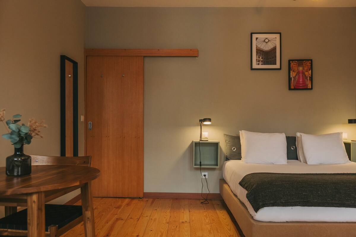 A bedroom with a bed, bedside tables, a nightstand, a wooden door, and a wall-mounted picture.