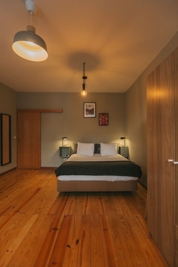 A bedroom with a large bed, wooden flooring, a wardrobe, and two bedside lamps. - Oporto Maison Sol   (Porto)