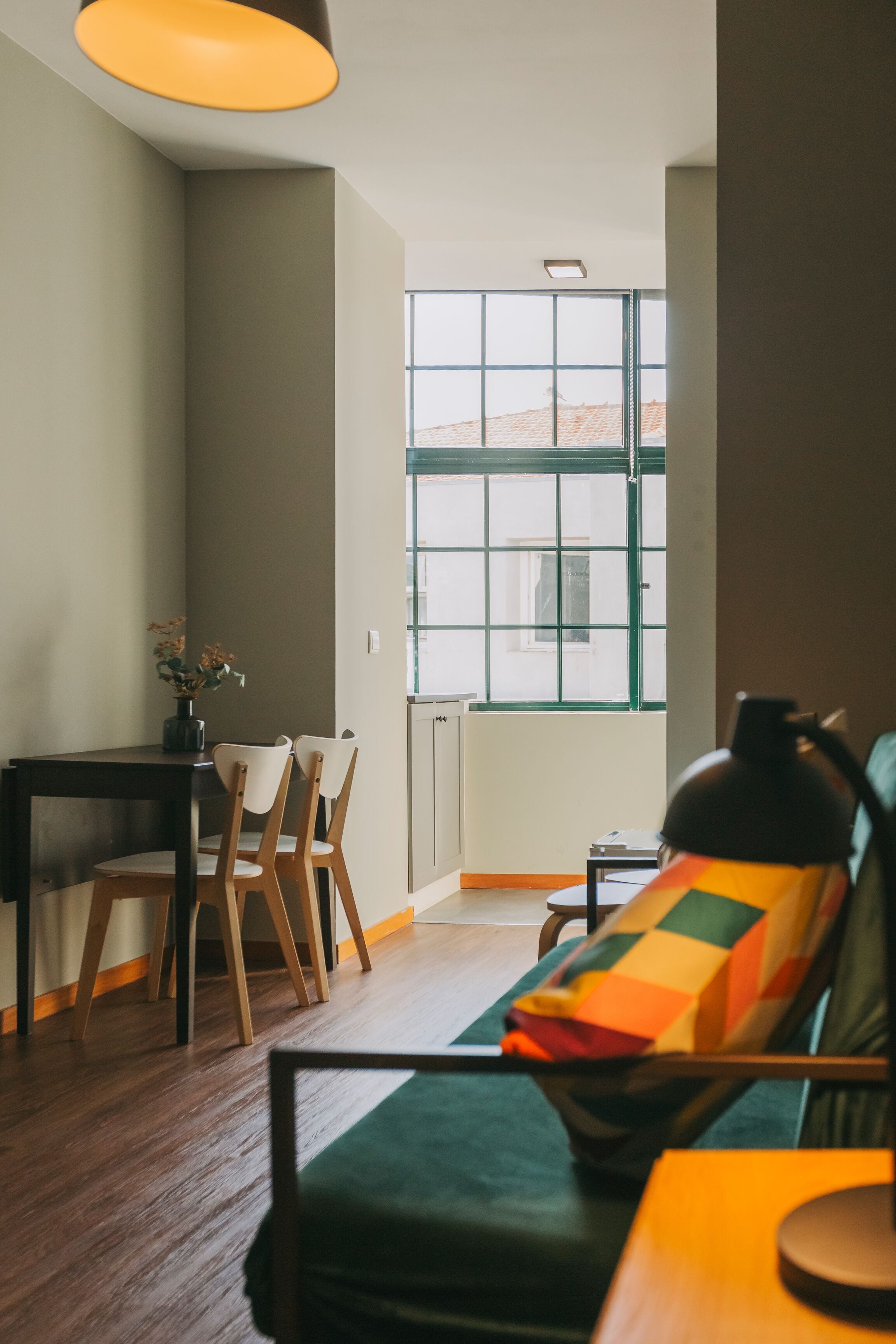 A cozy room with a sofa, a dining table with chairs, and a window with a view of buildings.