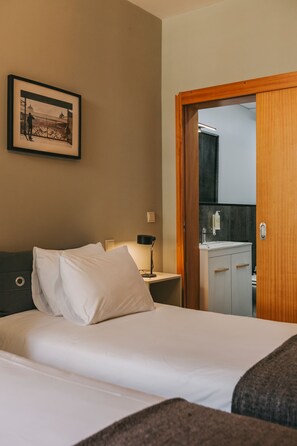 A hotel room with a bed, a nightstand with a lamp, a framed picture on the wall, and a bathroom visible through an open door. - Oporto Maison Sol   (Porto)