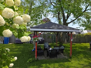 A covered patio area with outdoor furniture, a grill, and a garden with white flowers. - Lakeview Motel (Kincardine)