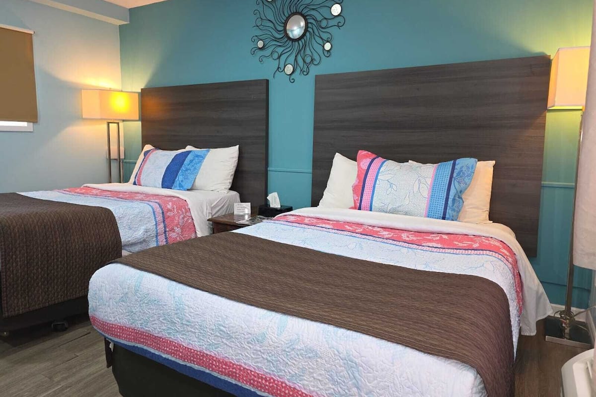 Quarto de hotel com duas camas, um objeto decorativo na parede e uma luminária de cabeceira.