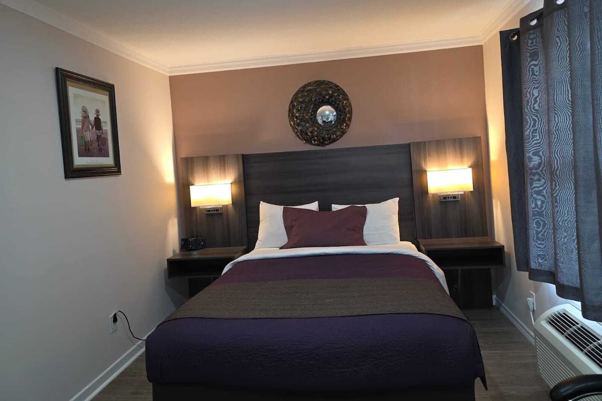 Quarto de hotel com uma cama grande, duas luminárias de cabeceira, um espelho fixado na parede e um quadro emoldurado.