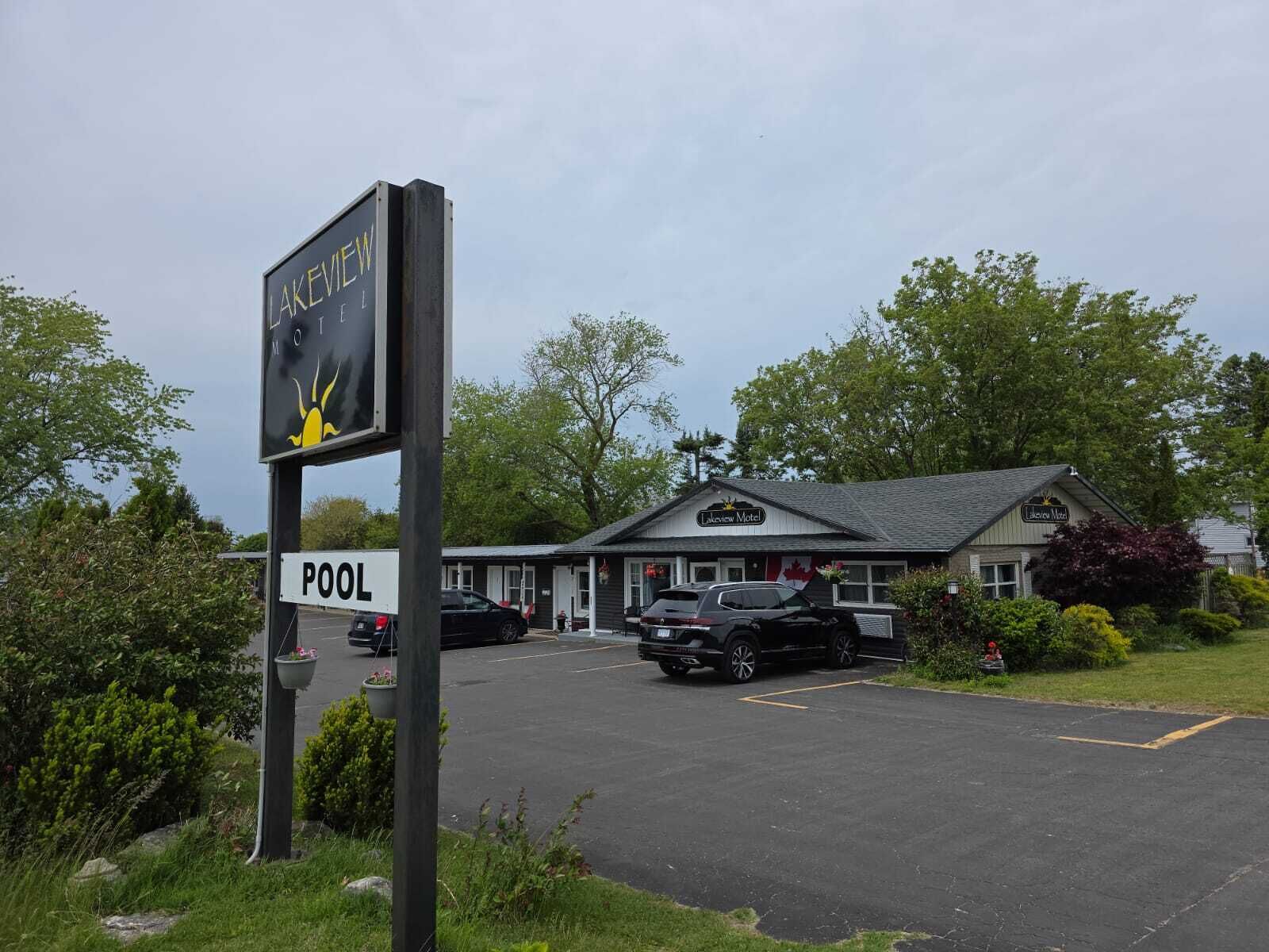 A motel with a sign indicating a pool, surrounded by greenery and parked cars.