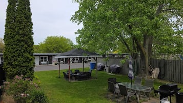 A backyard with a covered patio, outdoor seating, a barbecue grill, and a tall tree.