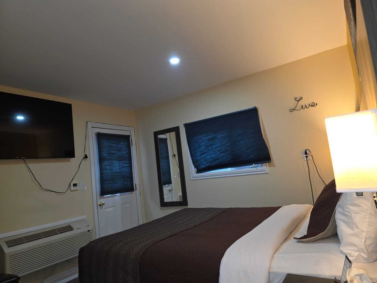 Une chambre d’hôtel équipée d’un lit, d’un téléviseur à écran plat fixé au mur, d’une fenêtre avec vue et d’un climatiseur mural.