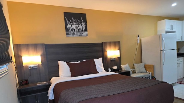 A hotel room with a large bed, bedside lamps, a small table, a chair, a refrigerator, and a wall-mounted picture. - Lakeview Motel (Kincardine)