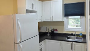 A compact kitchen with white cabinets, a refrigerator, a sink, and a window with a blind. - Lakeview Motel (Kincardine)