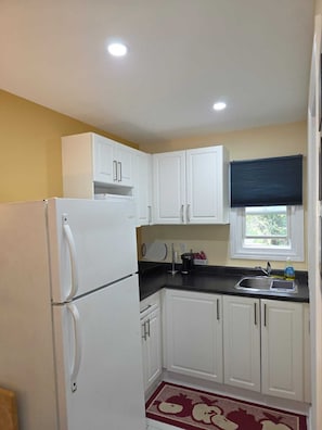 A compact kitchen with white cabinets, a refrigerator, a sink, and a window with a blind. - Lakeview Motel (Kincardine)