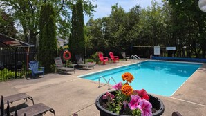 A swimming pool with lounge chairs, a potted plant with flowers, and a fenced area with trees. - Lakeview Motel (Kincardine)