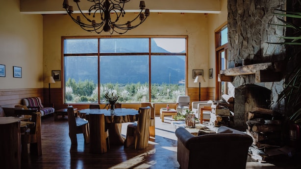 A spacious living room with a large window offering a mountain view, wooden furniture, and a stone fireplace. - Hotel Natura Patagonia (Puerto Varas)