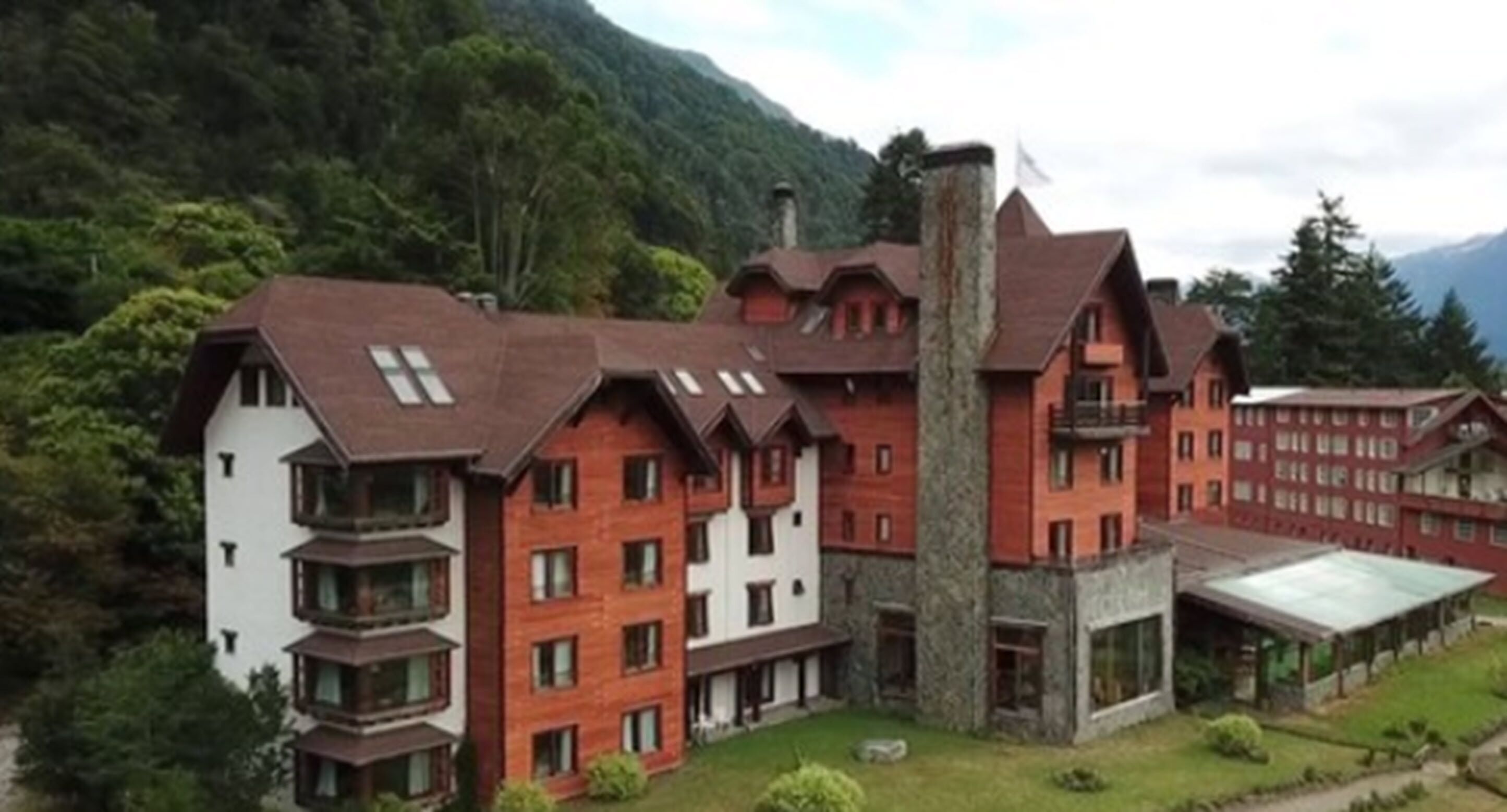 A multi-story hotel with a mix of red and white exterior walls, a prominent stone chimney, and a covered outdoor area.
