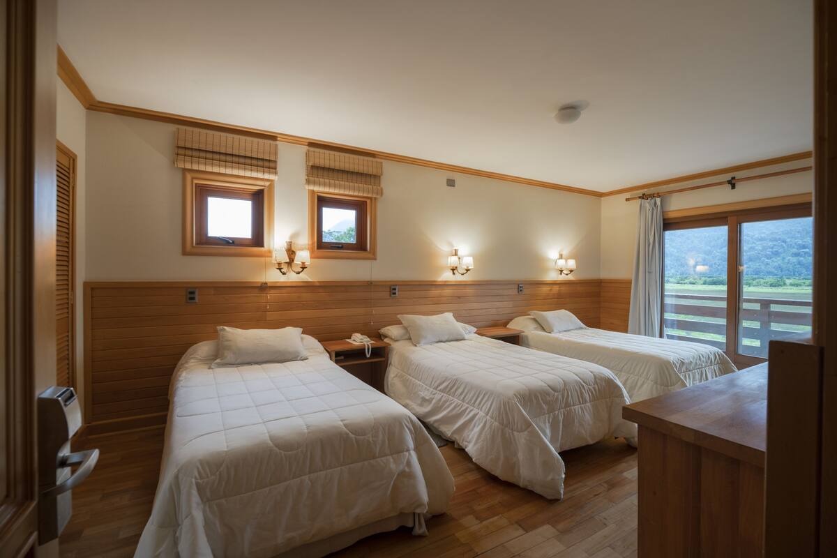 Ein Hotelzimmer mit zwei Betten, einem Holzkopfteil, Nachttischlampen, einem Schreibtisch und einem Fenster mit Blick ins Freie.