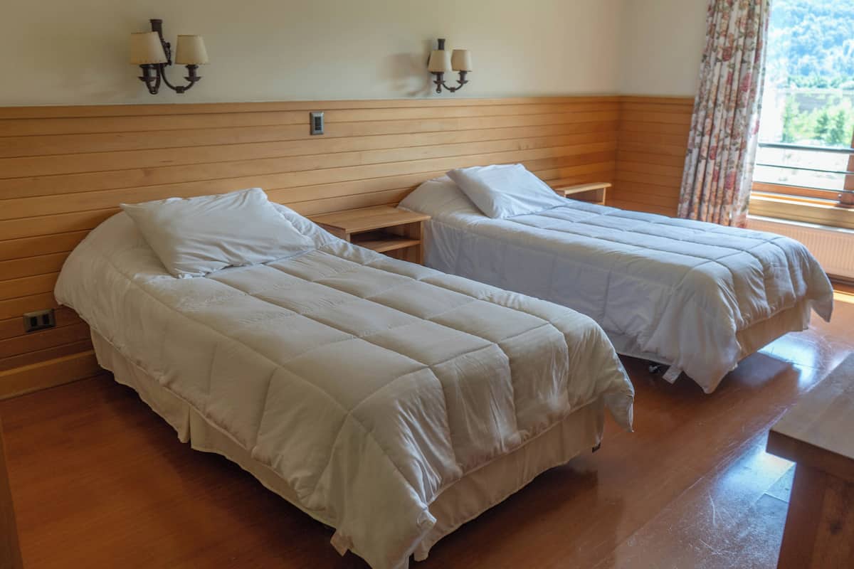 Ein Zimmer mit zwei Betten, einem Holzkopfteil, Nachttischen und Wandleuchten, sowie einem Fenster mit Blick.