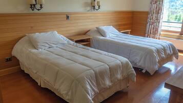Una habitación con dos camas, cabecero de madera, mesitas de noche, apliques de pared y una ventana con vistas.