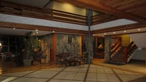 A spacious lobby with a high ceiling, wooden beams, a stone wall, and a staircase. - Hotel Natura Patagonia (Puerto Varas)