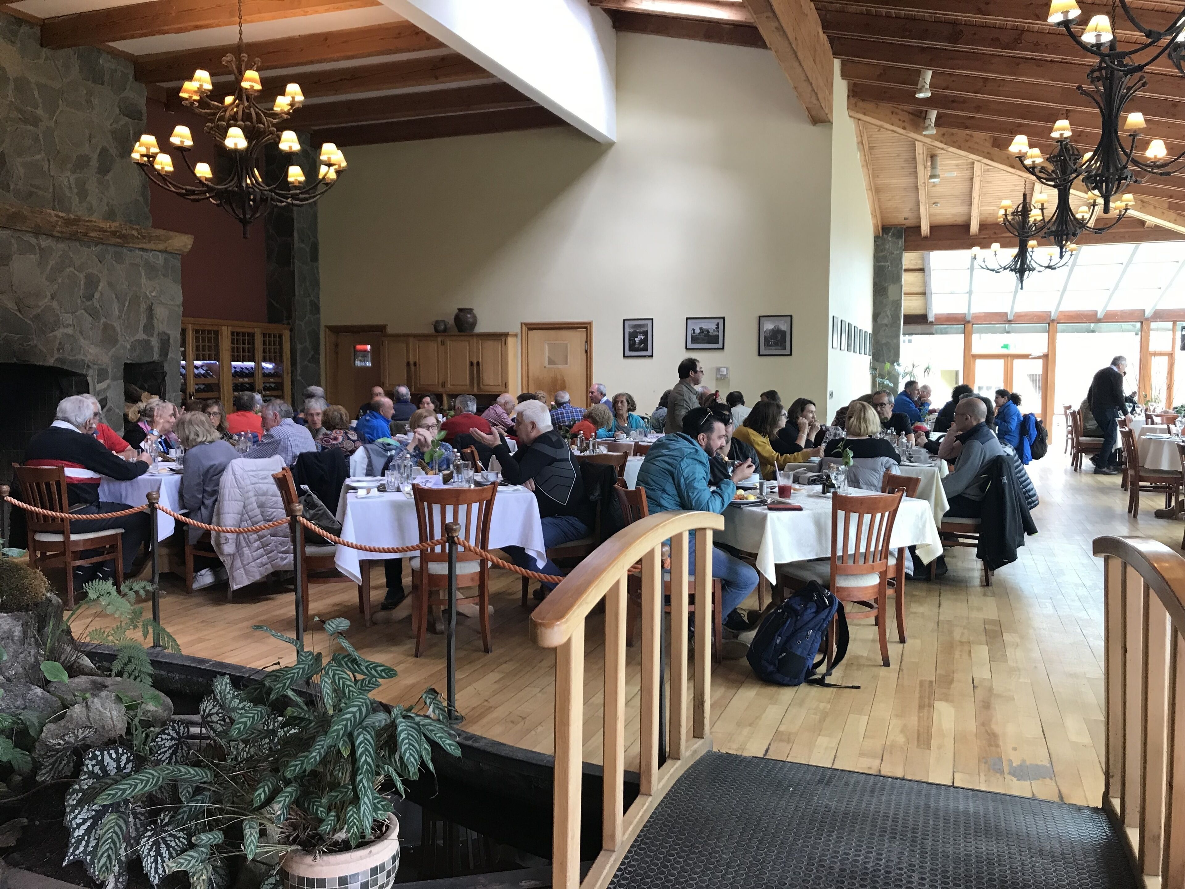 Un vaste espace dédié à la salle à manger, avec des tables et des chaises en bois, des murs en pierre et des lustres suspendus.