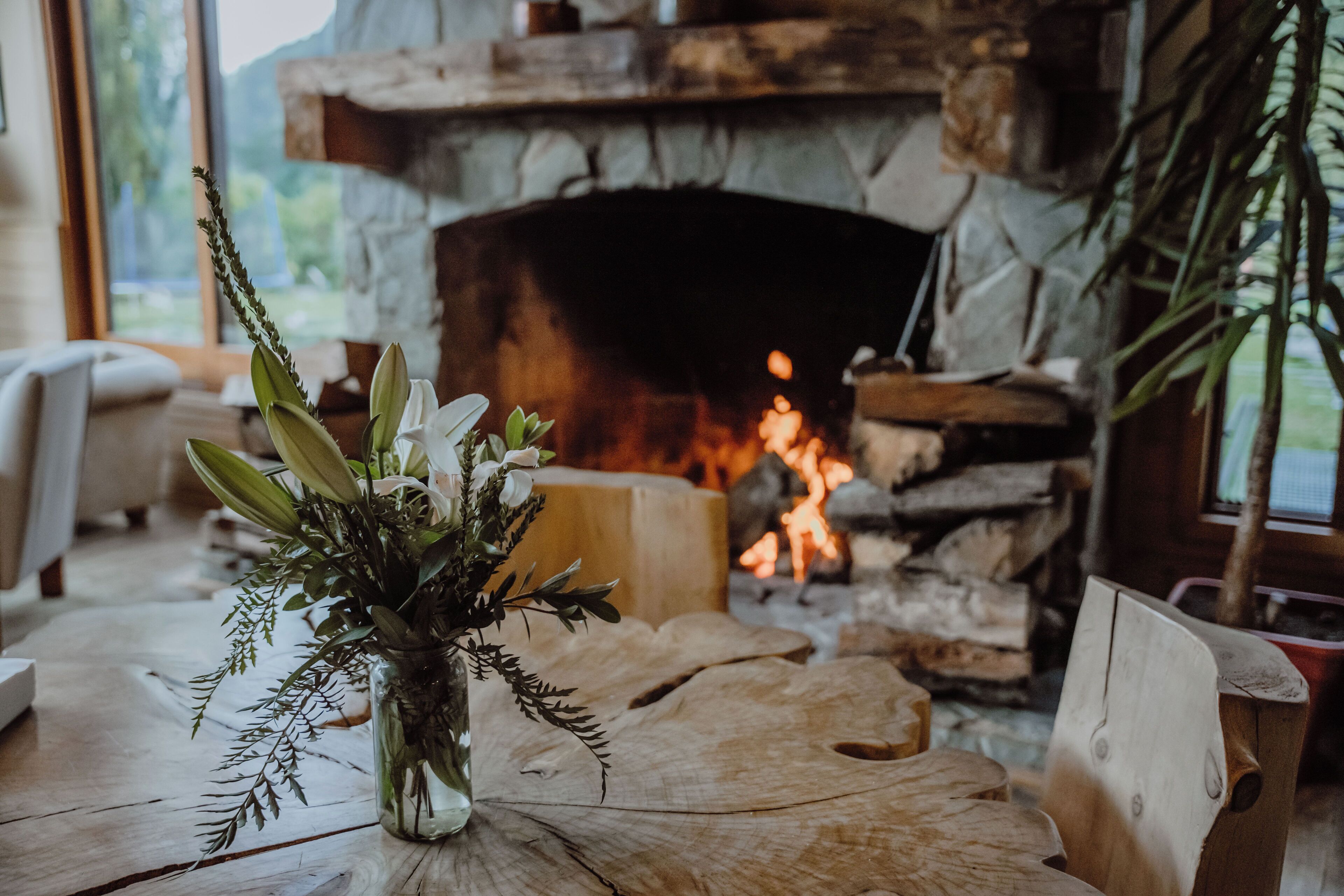 A rustic interior with a stone fireplace, wooden furniture, and a vase with flowers on a wooden table.