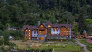 A large, multi-story hotel with a traditional architectural style, surrounded by lush greenery and mountains. - Hotel Natura Patagonia (Puerto Varas)