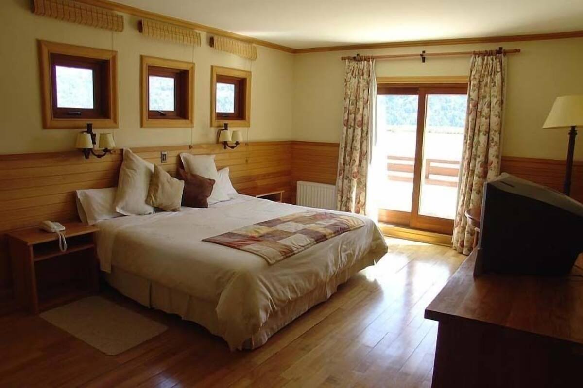 Ein Schlafzimmer mit einem großen Bett, einem Holzkopfstück, zwei Nachttischen, einem Schreibtisch und einem Fenster mit Vorhängen.