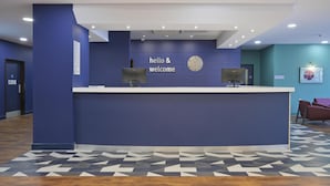 Zona de recepción con pared azul, un reloj y un cartel que dice 'hello & welcome'.