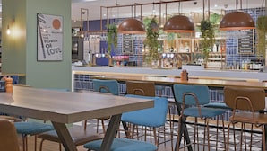 Un café moderno con una mesa de madera y sillas azules, un cartel de menú y plantas colgantes.