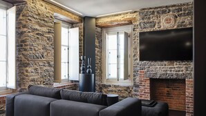 A modern living room with stone walls, a fireplace, a large flat-screen TV, and a sectional sofa. - Hôtel Maison du Fort (Québec City)