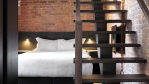 A modern room with a bed, a wooden staircase, and a brick wall. - Hôtel Maison du Fort (Québec City)
