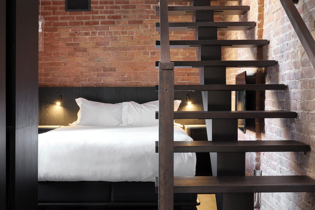 Ein modernes Zimmer mit einem Bett, einer Holztreppe und einer Backsteinwand.